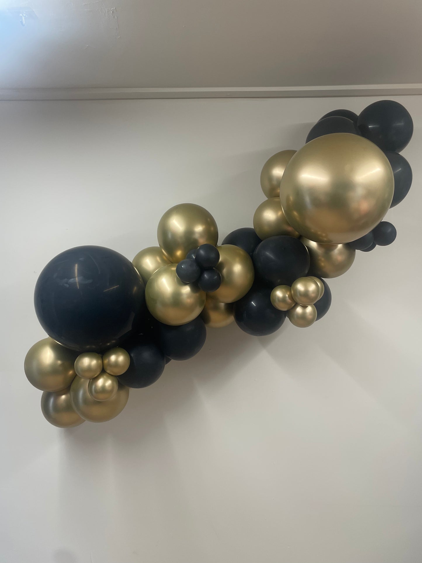 Balloon arch with black and gold balloons on a white wall