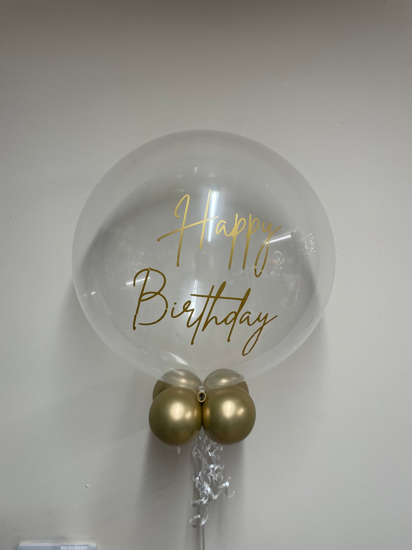 Clear balloon with 'Happy Birthday' text and gold balloons on a white background