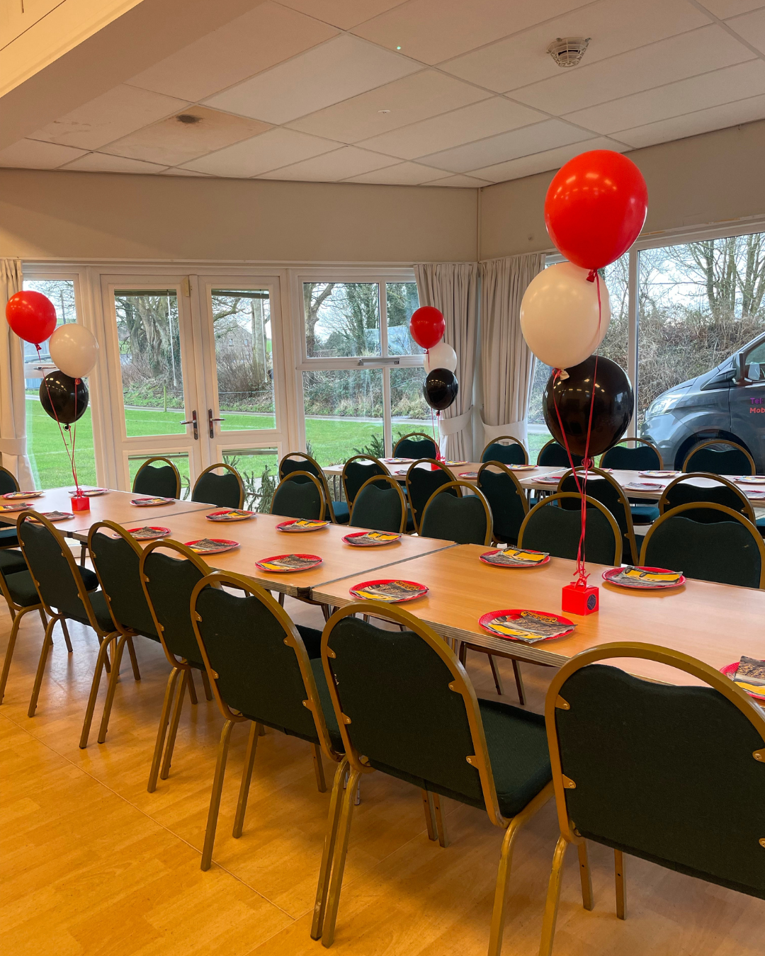 Dining room with tables, chairs, and balloons in a room with large windows.