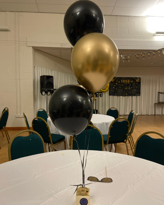 Black and gold balloons on a table with chairs and a stage in the background
