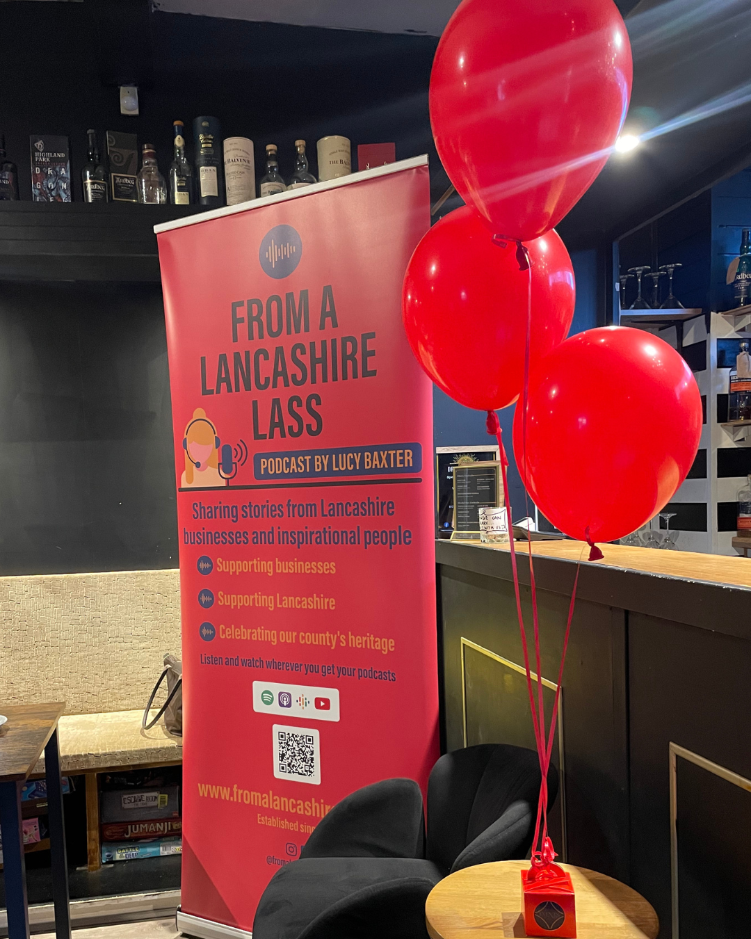 Promotional banner for 'From a Lancashire Lass' podcast with red balloons in a room setting.