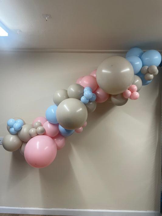 Balloon arch with pastel balloons against a plain wall