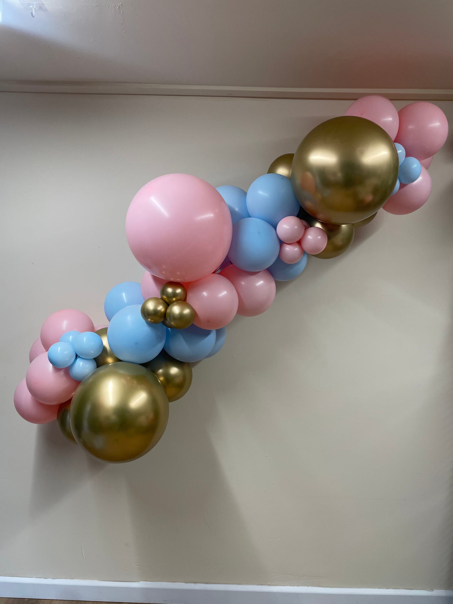 Balloon arch with pink, blue, and gold balloons against a plain background
