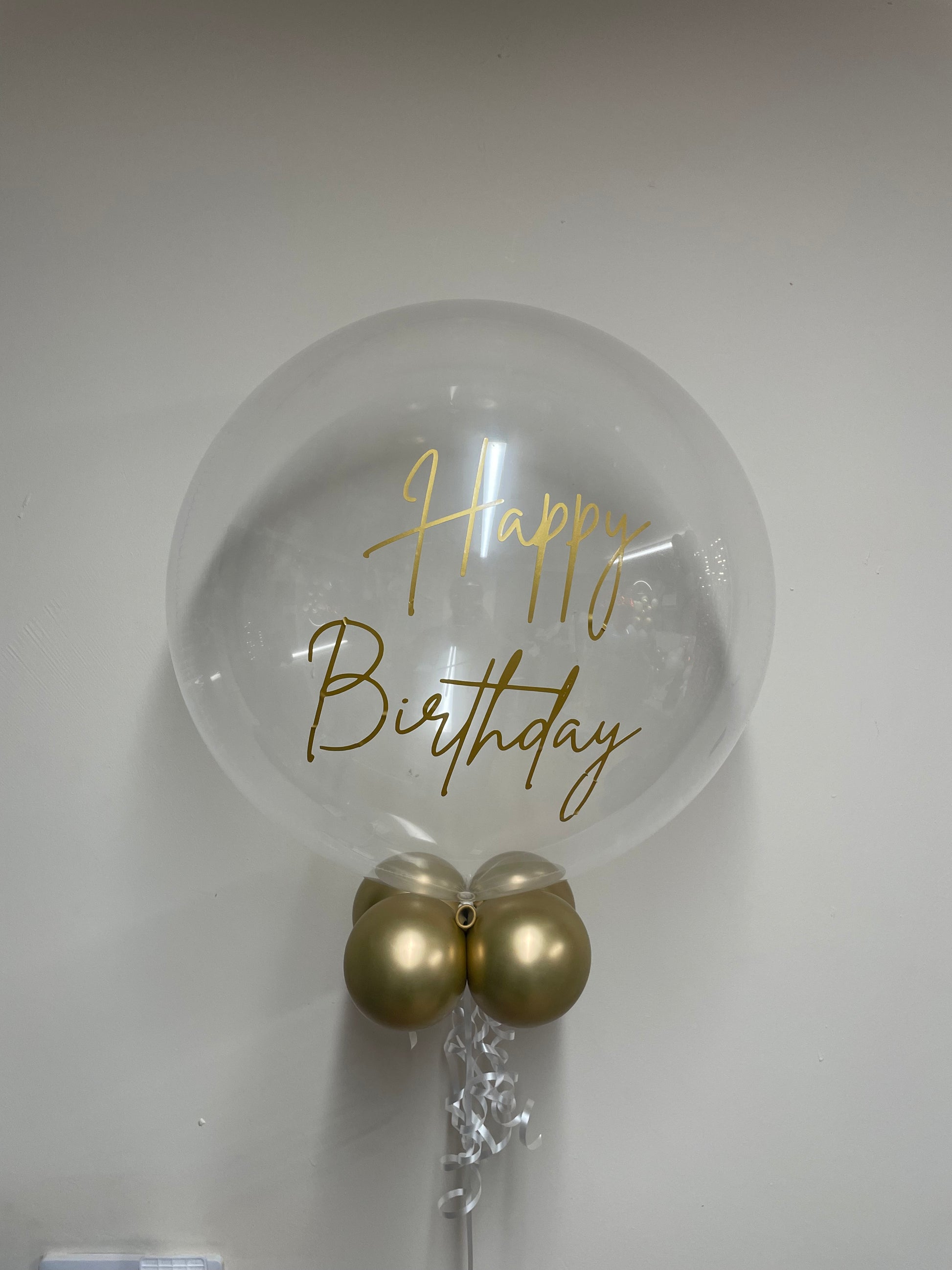 Clear balloon with 'Happy Birthday' text and gold balloons on a white background