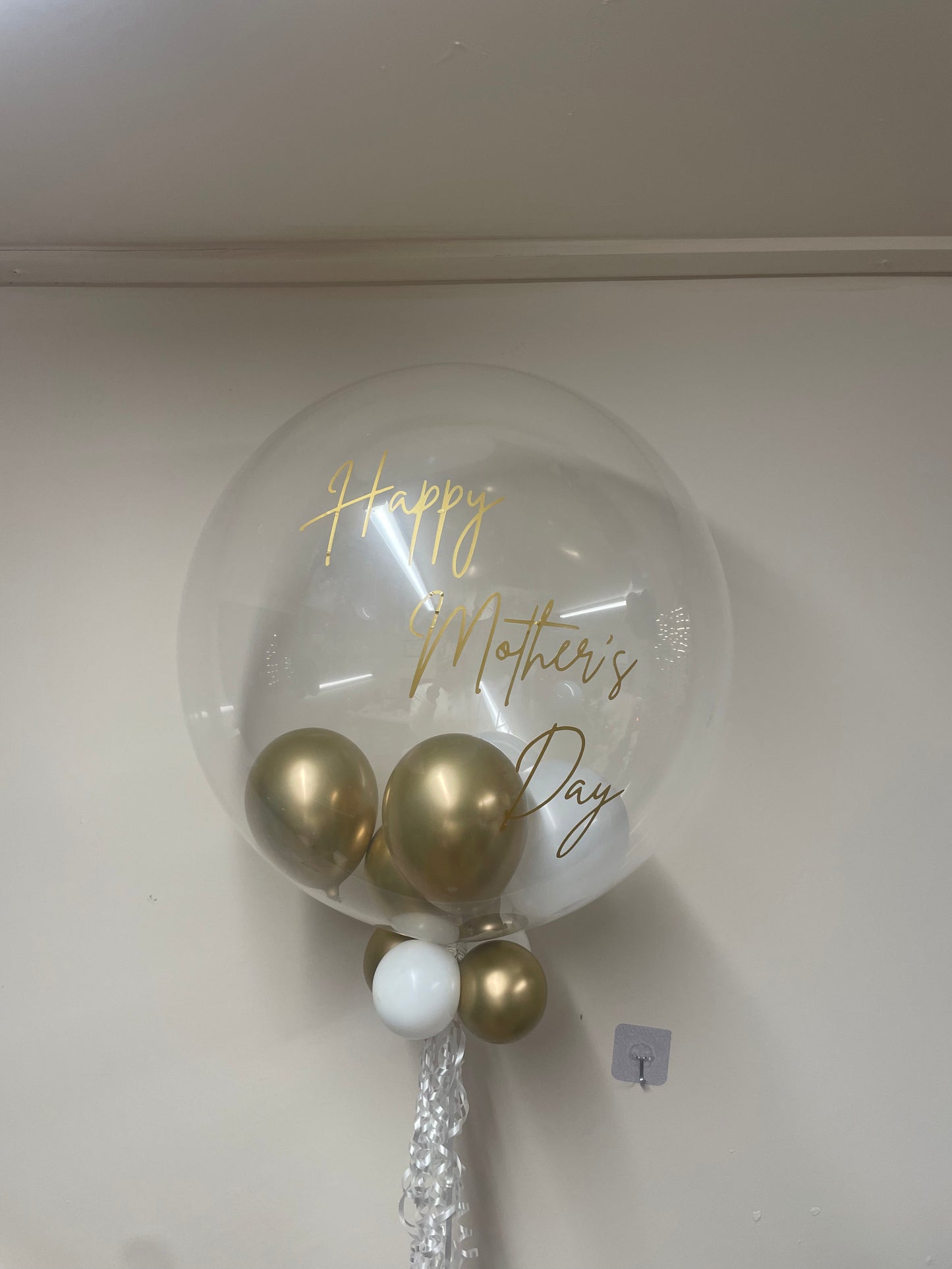 Clear balloon with gold and white balloons inside, featuring 'Happy Mother's Day' text on a white background.