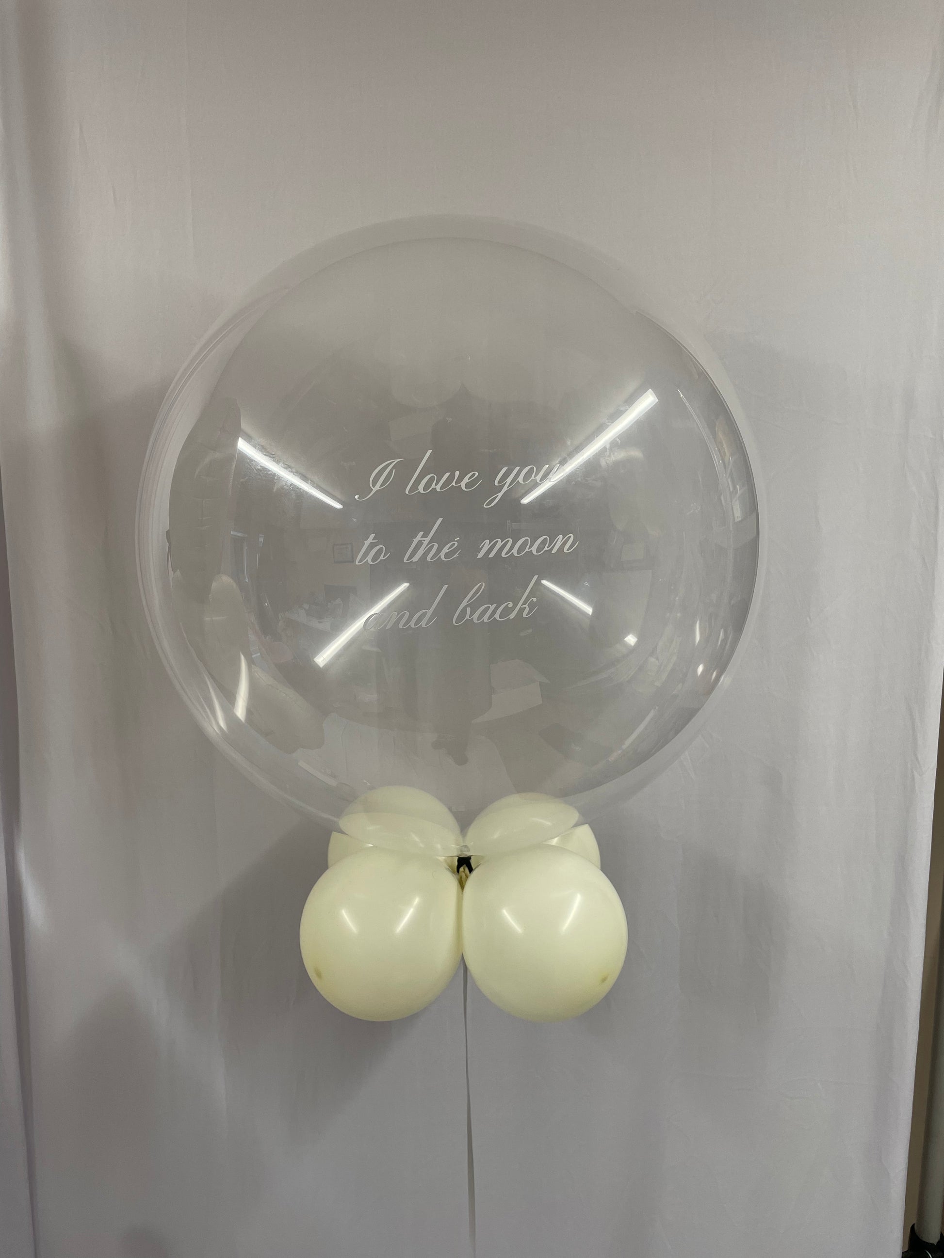 Clear balloon with white text saying 'I love you to the moon and back' and smaller white balloons attached on a white background
