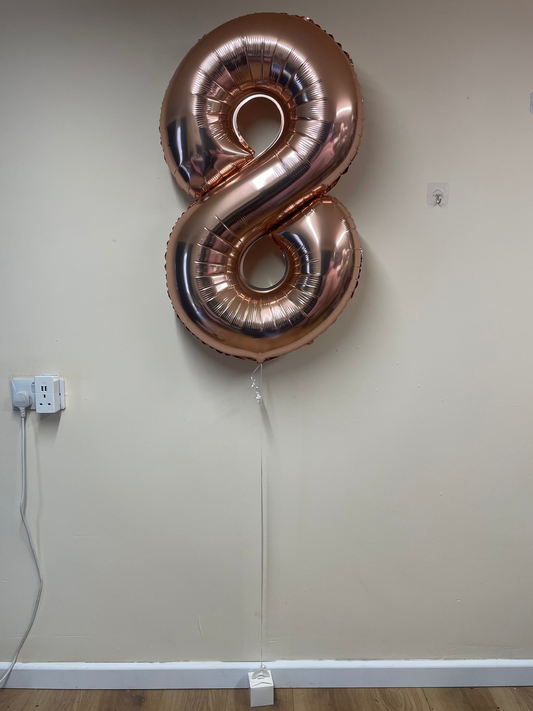 Rose gold number 8 balloon against a plain wall.