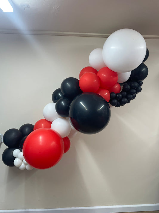 Balloon arch with red, black, and white balloons against a plain wall.