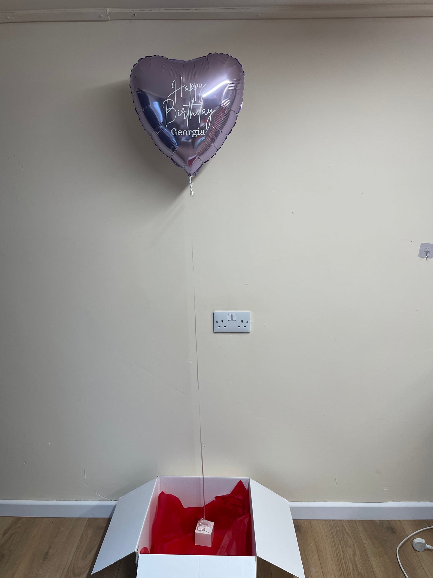 Heart-shaped balloon with 'Happy Birthday Georgia' text in a white box against a plain wall.