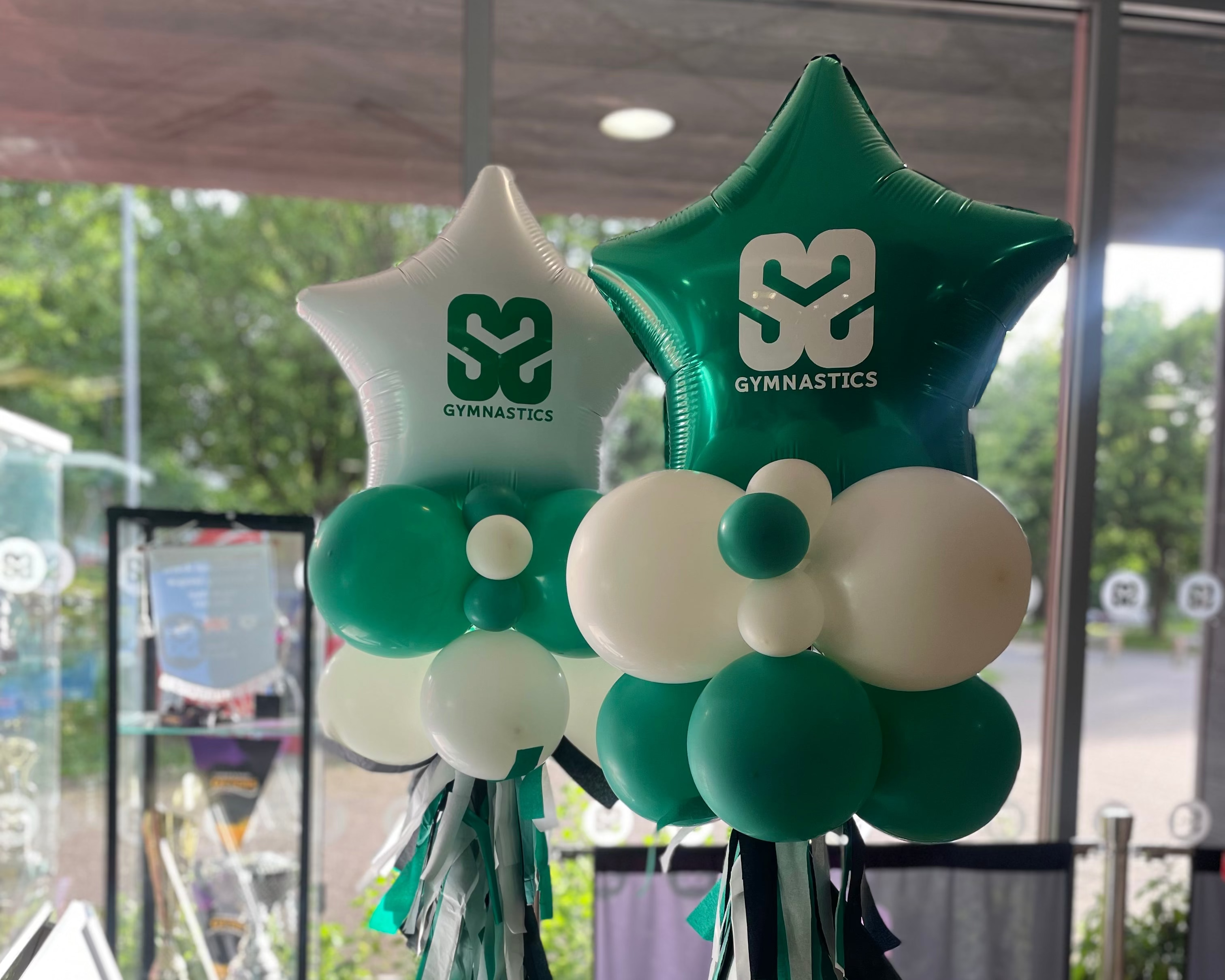 Decorative balloons shaped like stars with SM Gimnastics logos in a room with large windows.