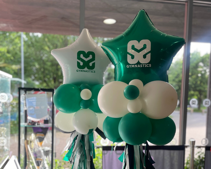 Decorative balloons shaped like stars with SM Gimnastics logos in a room with large windows.