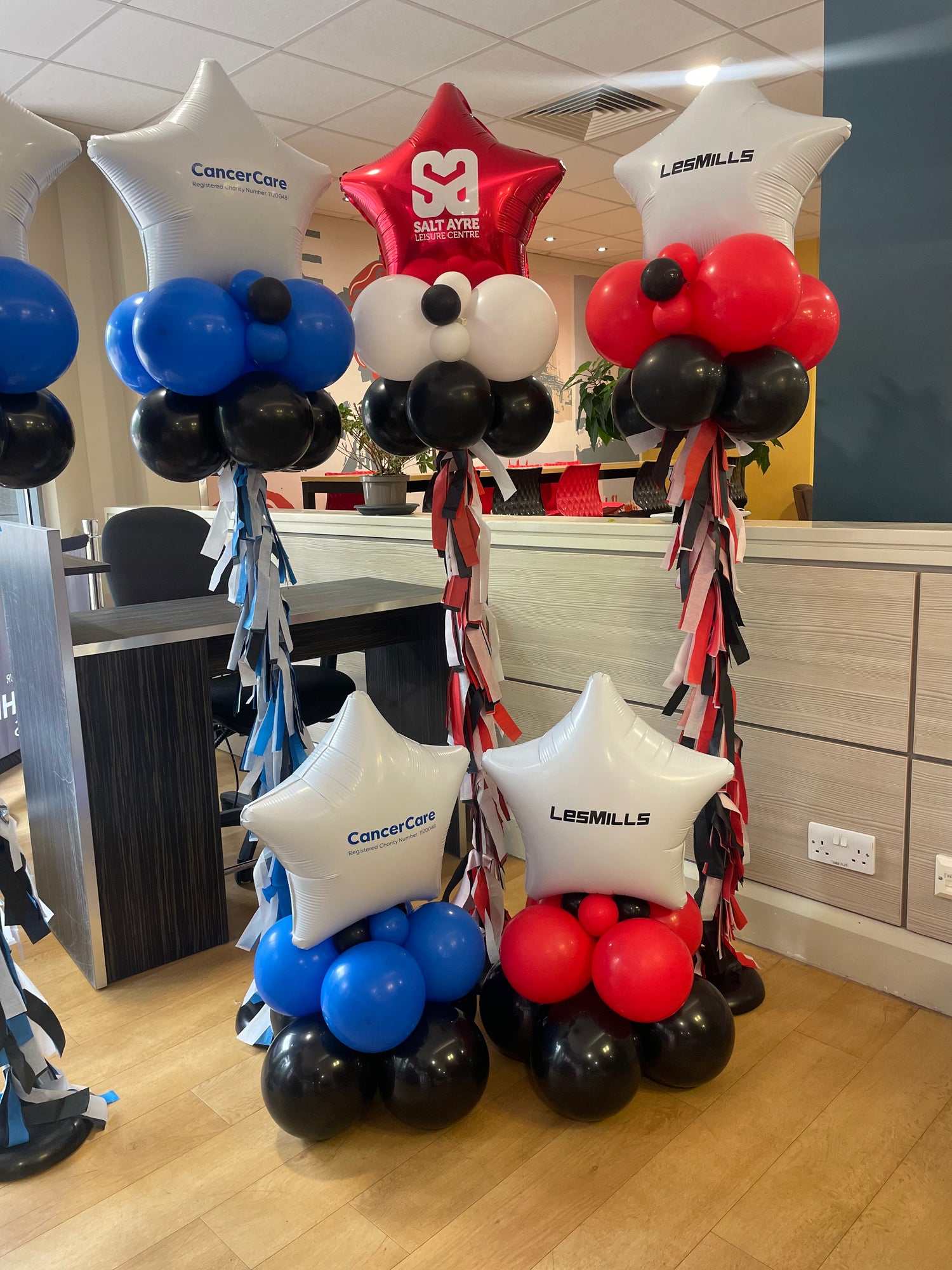 Decorative balloon arrangements with CancerCare and Les Mills logos in a room setting.